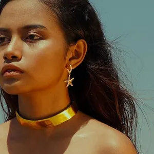 Detail of golden starfish hoop earrings and polished thick choker worn by a model