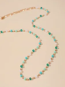 Détail d'un collier de perles dorées avec cubes verts et finition métal brillant