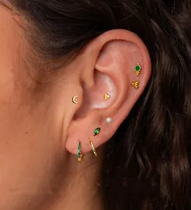 Close-up of gold star and moon earrings set with green cubic zirconia on model ear