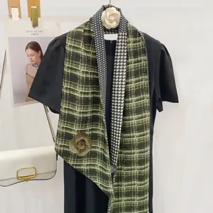 Détail d'une écharpe vert foncé avec broderie de camélia et motif classique en chevrons