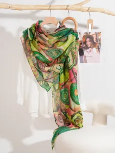 Artistic scroll print silk scarf in green and pink on a rustic branch display