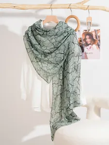 Dettaglio di sciarpa verde chiaro con motivo marmoreo drappeggiata su un ramo in legno