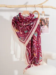 Dettaglio di sciarpa rossa con motivo paisley e bordo beige su gruccia di legno