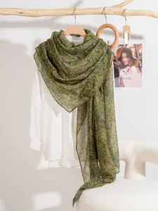 Detail of green floral chiffon scarf texture hanging on a minimalist wooden rack