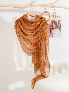 Detail of floral print scarf hanging on a wooden hanger against a minimalist background
