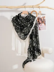 Dettaglio di una sciarpa lunga e sottile con motivo paisley bianco e oro su nero