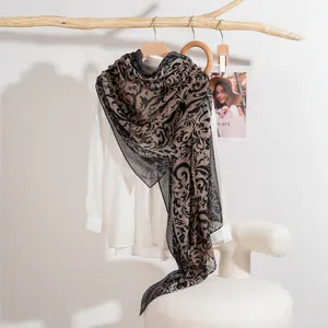 Lightweight brown scarf with black vine prints hanging on a wooden display stand