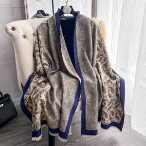 Scialle paisley verde oliva con frange su gruccia vicino a un divano bianco