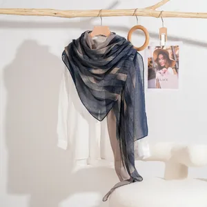 Sciarpa leggera a righe sfumate blu scuro e taupe appesa a un ramo di legno naturale