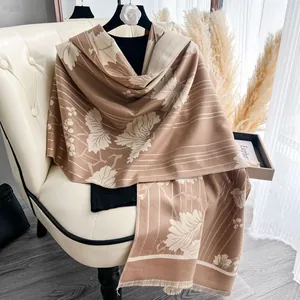 Dettaglio scialle jacquard floreale con frange e motivi a foglia su una sedia beige