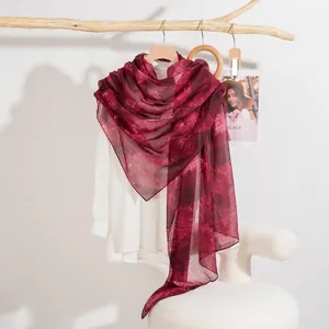 Sciarpa bordeaux con stampa sfumata appesa a una gruccia in legno con camicia bianca