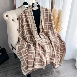 Detail eines weichen Strickschals in Beige und Braun mit feinen Quasten auf dem Ledersofa