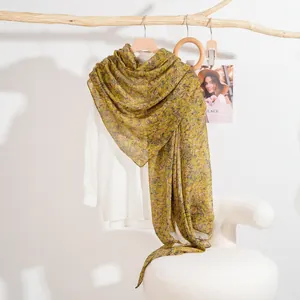 Floral print long scarf in yellow and green chiffon hanging on a wooden hanger with white shirt