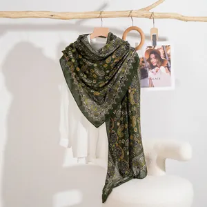 Sciarpa verde scuro con motivo paisley giallo appesa a una gruccia su sfondo bianco