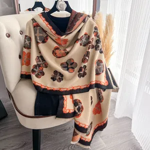 Détail d'une écharpe d'hiver en cachemire avec imprimé floral orange et bords à pompons
