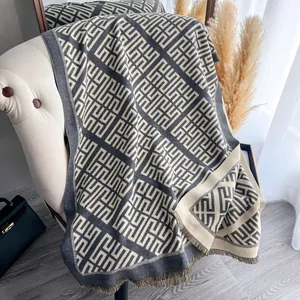 Dettaglio macro dello scialle geometrico grigio e beige con nappe e tessuto morbido