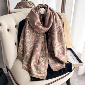Detail of tan paisley pashmina shawl with fringe edges and white camellia brooch