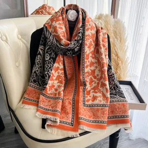 Dettaglio del motivo floreale damascato e frange sullo scialle in cashmere arancio e nero