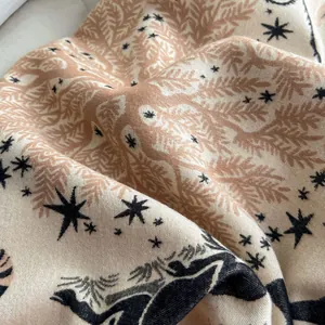 Dettaglio di una morbida sciarpa beige con stampe floreali e sagome di cervi