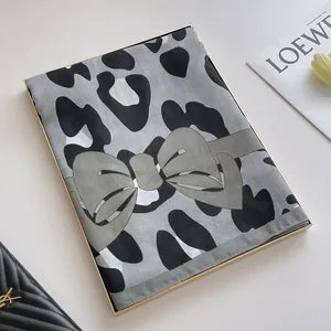 Gros plan de l'écharpe en lin léopard avec motif nœud vert dans sa boîte cadeau
