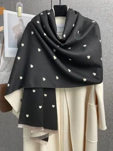 Dettaglio sciarpa nera a pois con cuori e frange sottili su un cappotto bianco