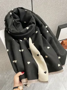 Dettaglio della morbida trama in finto cashmere con motivi a cuore e bordi con frange