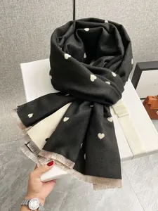 Dettaglio sciarpa nera a cuori con nappe dorate presentata su una confezione regalo bianca