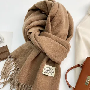 Dettaglio della sciarpa di cashmere cammello con frange ed etichetta su sfondo caldo