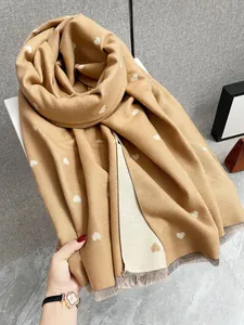 Dettaglio della sciarpa in cashmere color cammello con cuori bianchi e morbide frange