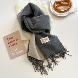 Dettaglio della sciarpa stile cashmere grigio e beige con frange ed etichetta del marchio