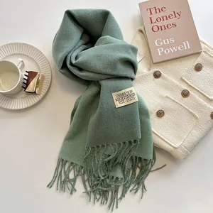 Dettaglio di sciarpa verde salvia effetto cashmere con frange ed etichetta tessuta