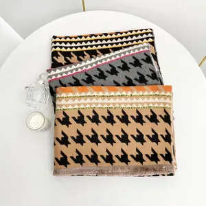 Tre sciarpe pied-de-poule tipo cashmere con frange su tavolo bianco in ambiente elegante