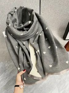 Dettaglio macro della sciarpa grigia con motivo jacquard a cuore e rifiniture con frange