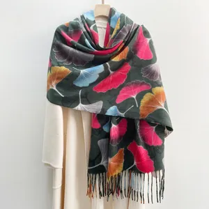 Green scarf with maple leaf print and tassels styled on a white wool coat