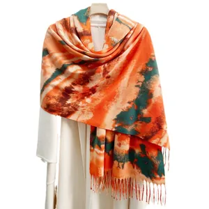 Sciarpa tie-dye effetto cashmere con nappe appesa a una gruccia sopra un cappotto color beige
