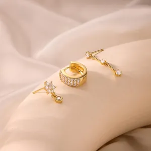 Close-up of gold brass earrings set with zircons featuring flower and linear designs