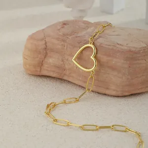 Golden paperclip chain necklace with a large hollow heart pendant on a stone background