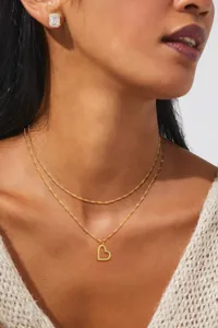 Detail shot of double-layered gold heart necklace and square pave stud earrings on a model