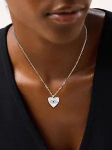 Detail of silver heart pendant necklace with evil eye motif and blue stone on neck