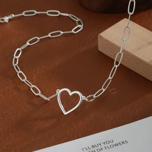 Macro detail of silver paperclip chain necklace with hollow heart pendant on leather background