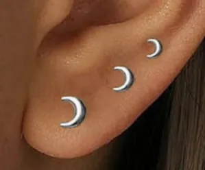 Detailed close-up of three silver crescent moon stud earrings in varying sizes on ear