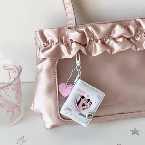 Close-up of a white mini heart-window photo album keychain on a pink satin ita bag