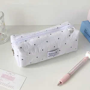 Detailopname van een witte polkadot etui met ritssluiting en een geweven merklabel erop