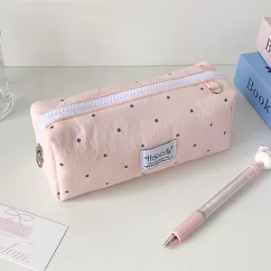 Detail van roze stippen etui met witte rits en blauw geweven label op een wit bureau