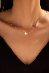 Close-up of a minimalist single white pearl pendant on a delicate gold chain necklace