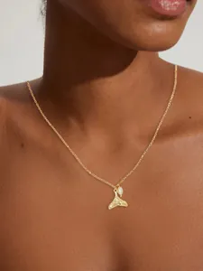 Detail of gold whale tail pendant and pearl necklace worn on model neck