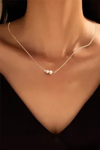 Close-up of elegant gold chain necklace featuring three round white pearls on a model
