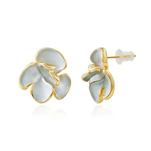 Macro view of gold-plated floral earrings with blue enamel petals and textured details