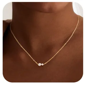 Detail van vergulde ketting met dubbele witte parelhanger gedragen door een model
