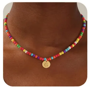 Gros plan de la lettre G gravée sur pendentif doré avec collier de perles colorées
